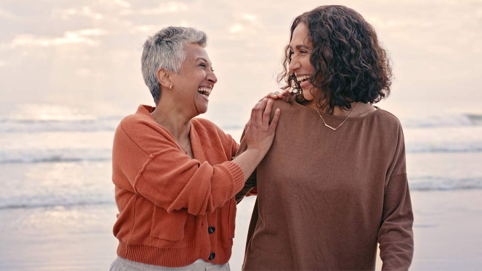 middle aged mother and daughter walking and laughing on the beach