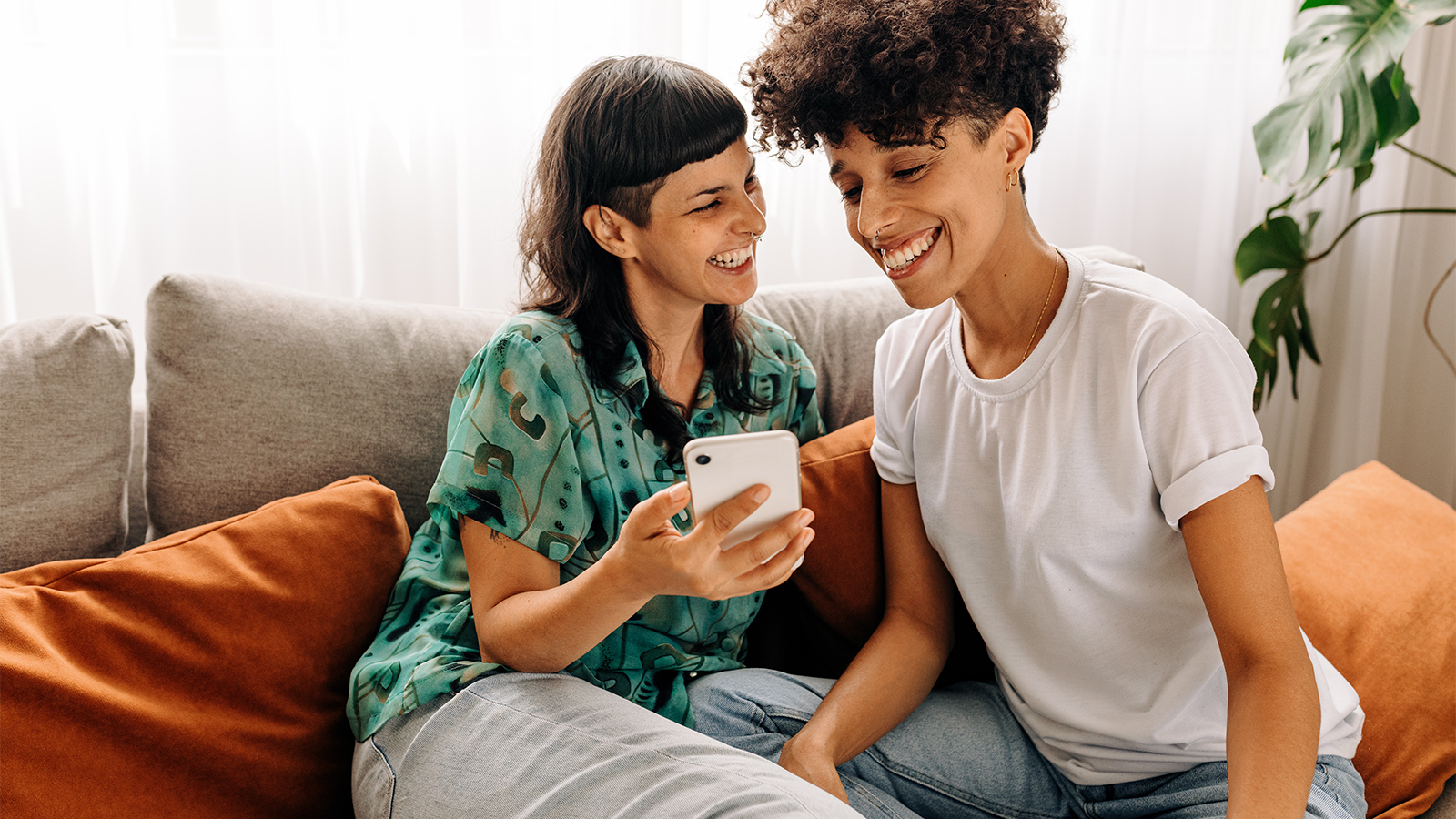 A female couple in their 30s looking at a cell phone and smiling