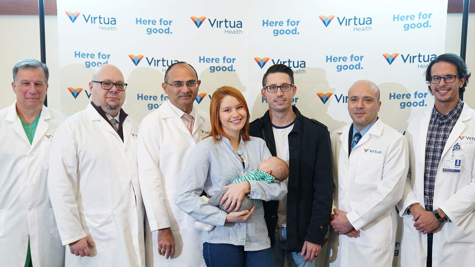 group of Virtua Health doctors in lab coats standing with father and mother holding a newborn baby