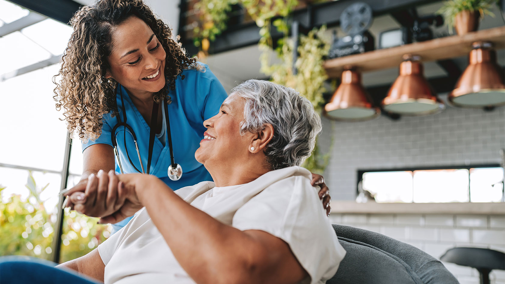 Female clinician holds the hand of an older female patient who is seated in an atrium