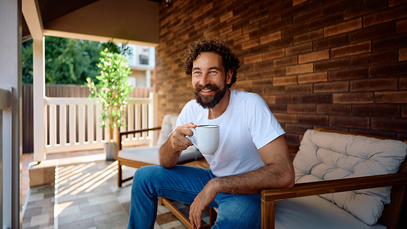 Mid-40s male smiles and sips coffee on a covered porch