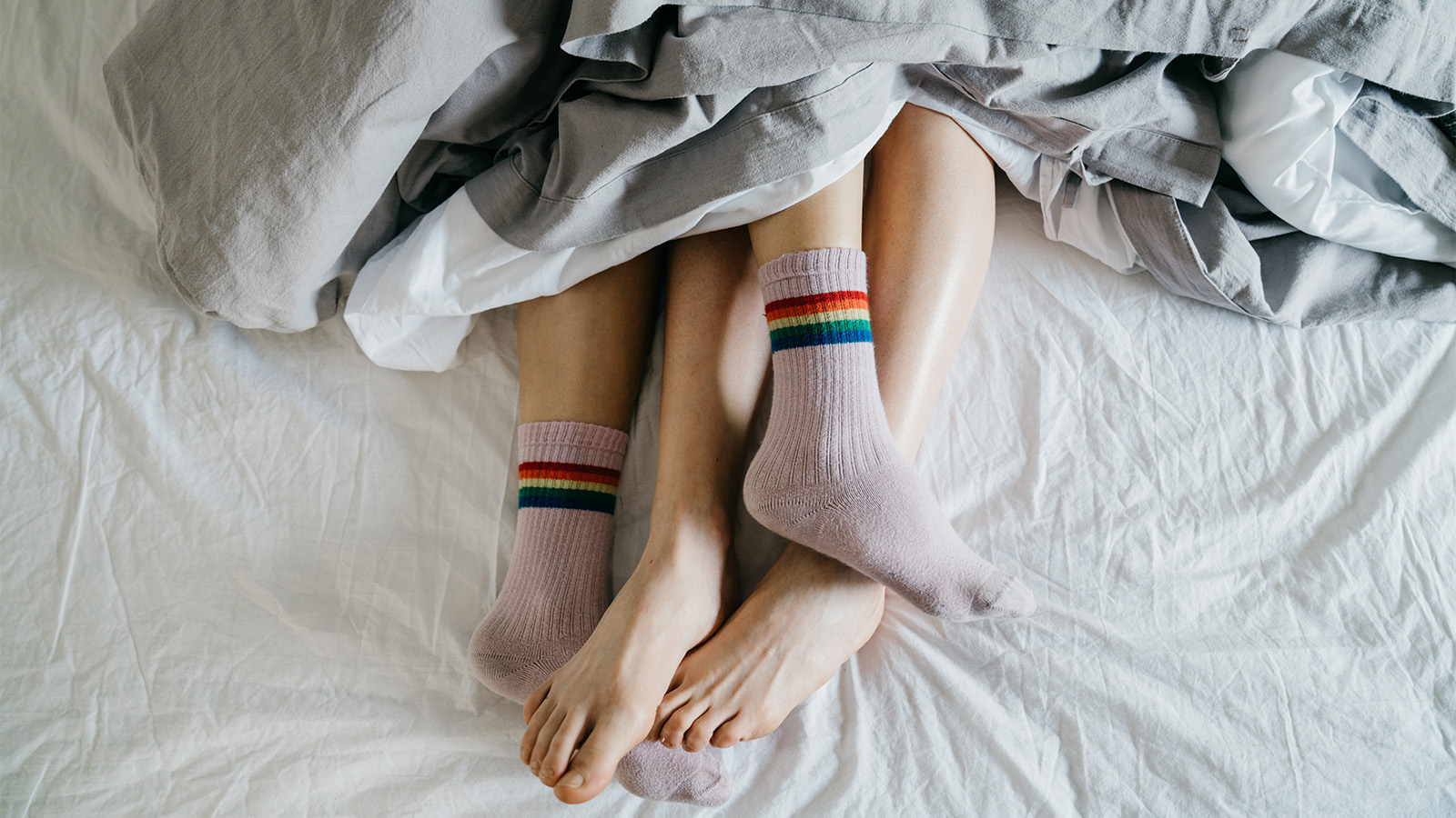 A couple shown in a bed, with only legs visible and their feet poking out from under blankets