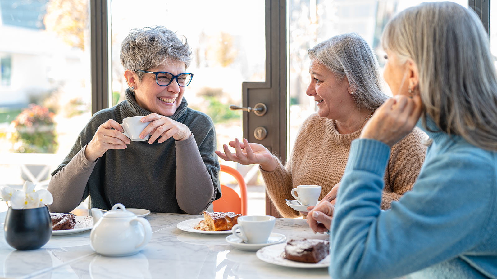 group of 3 older women talking while sharing dessert and coffee at a restaurant