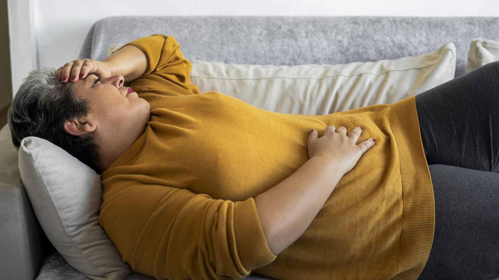 woman laying on the couch holding her stomach in pain