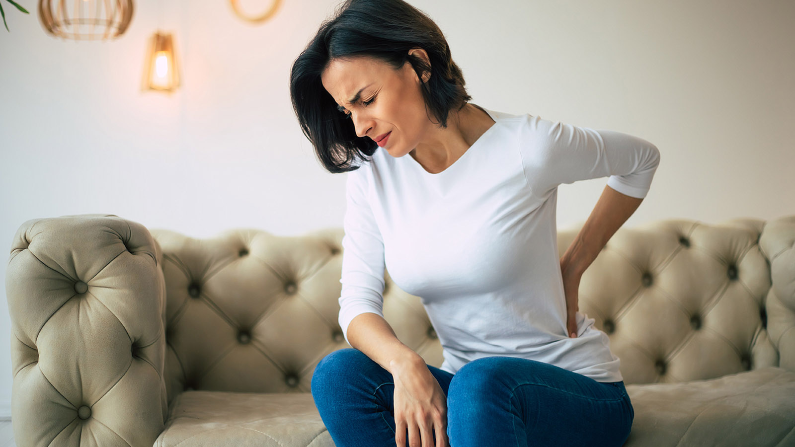 woman sitting on the couch holding her lower back in pain