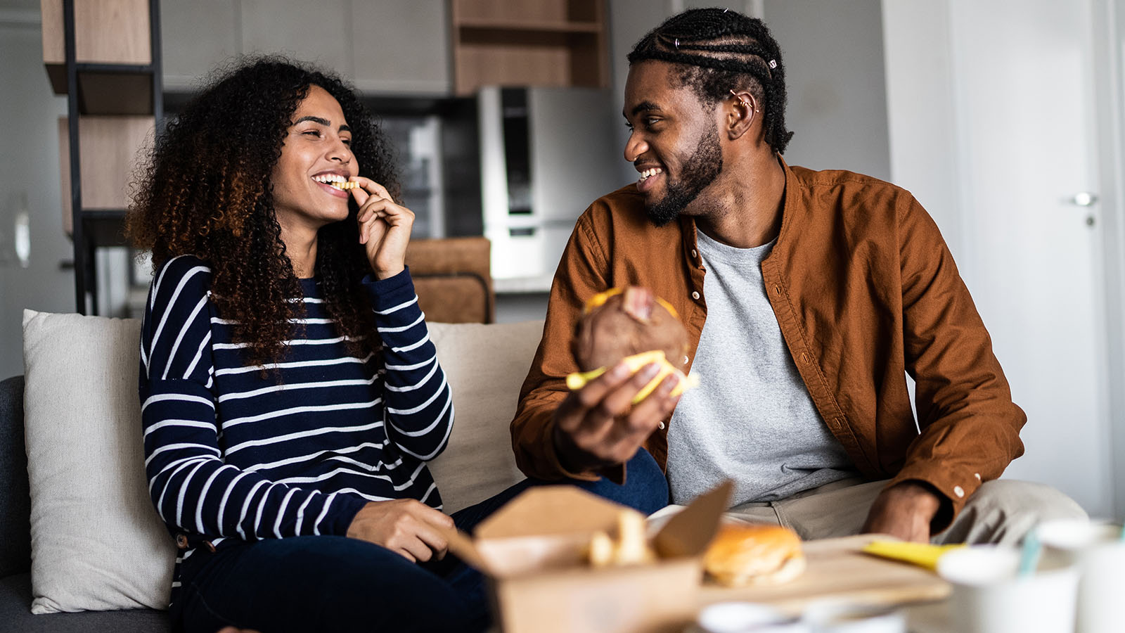 young couple enjoying burgers and fries at home