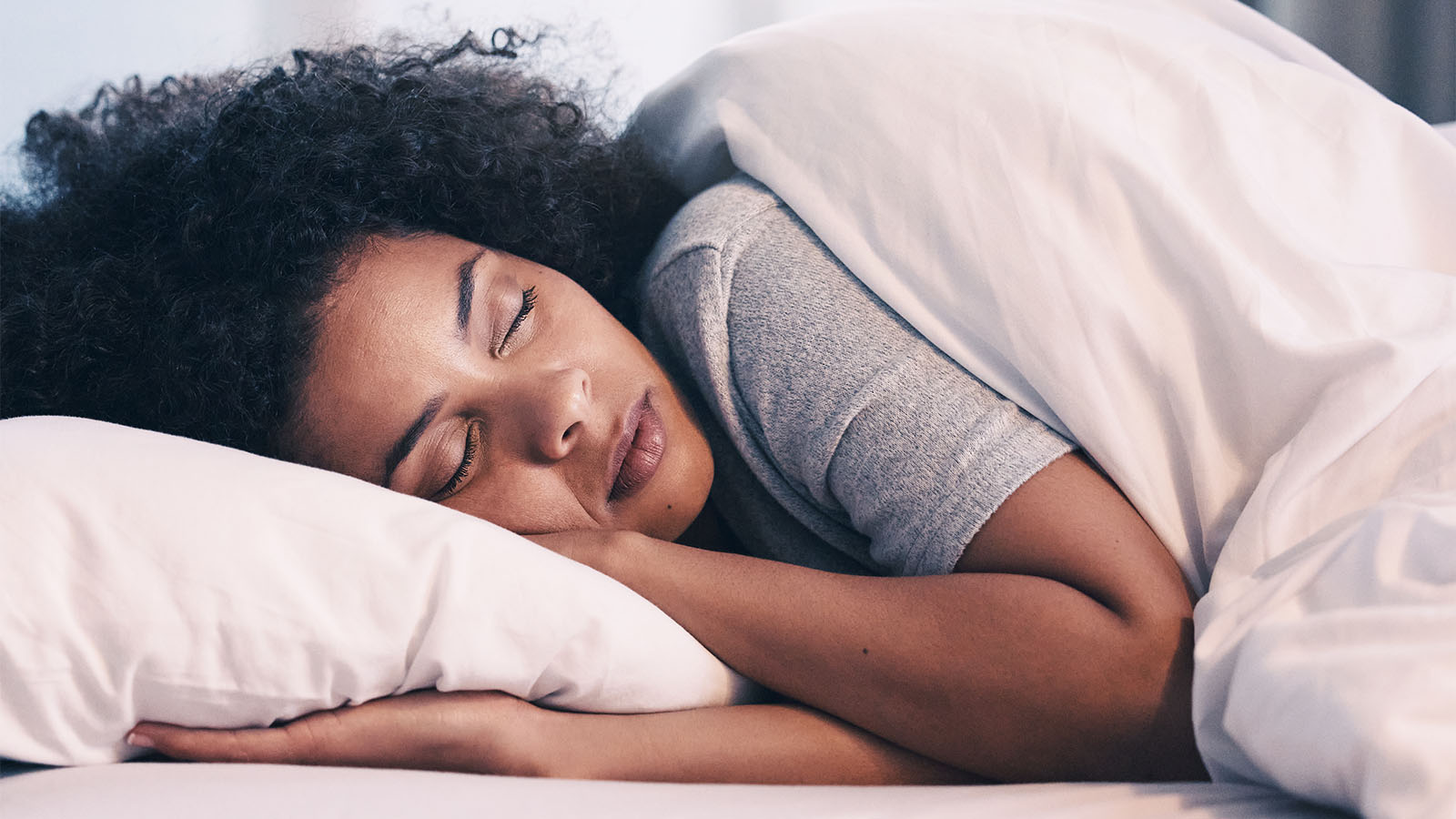 woman laying in bed covered with blanket and hugging pillow