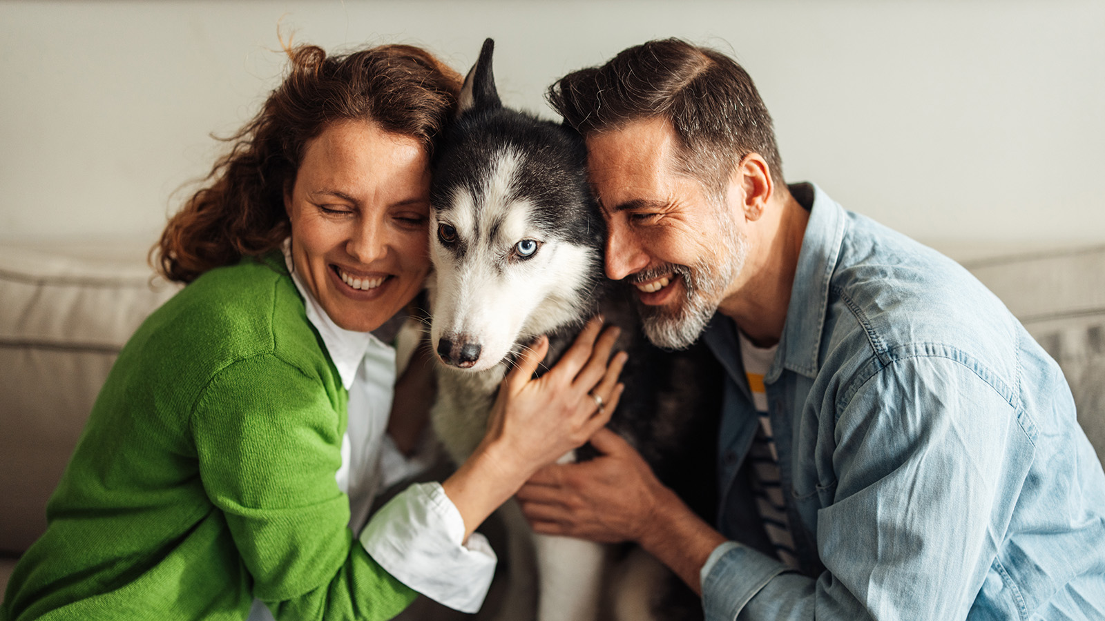 Couple in their 40s hugging a dog and smiling on the couch