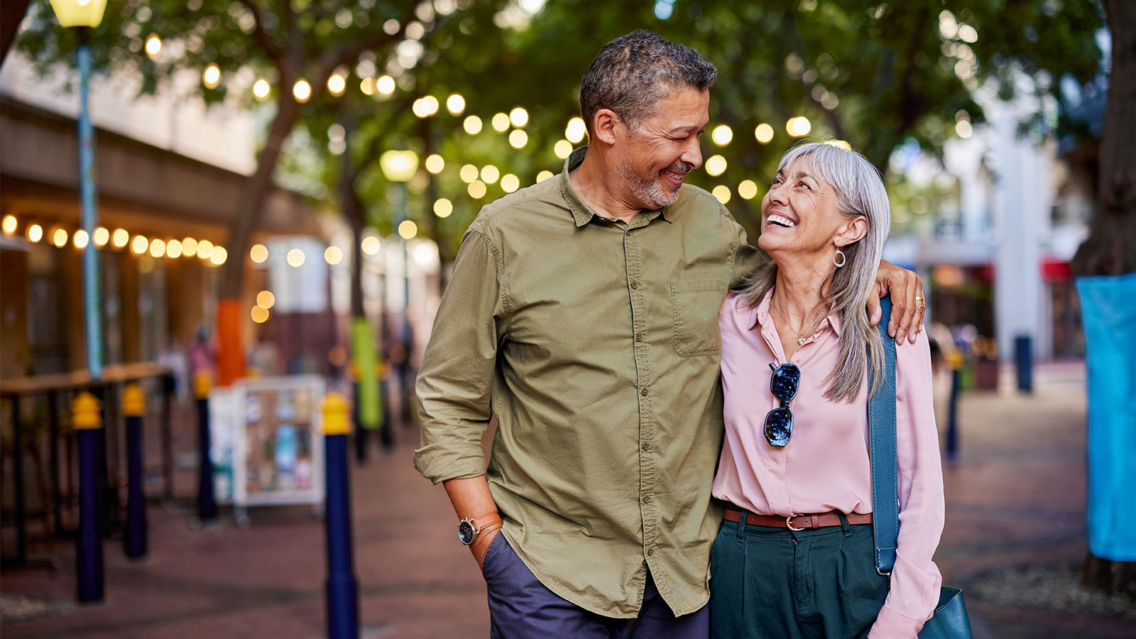 Older couple strolling along a street lined with trees, shops, and restaurants