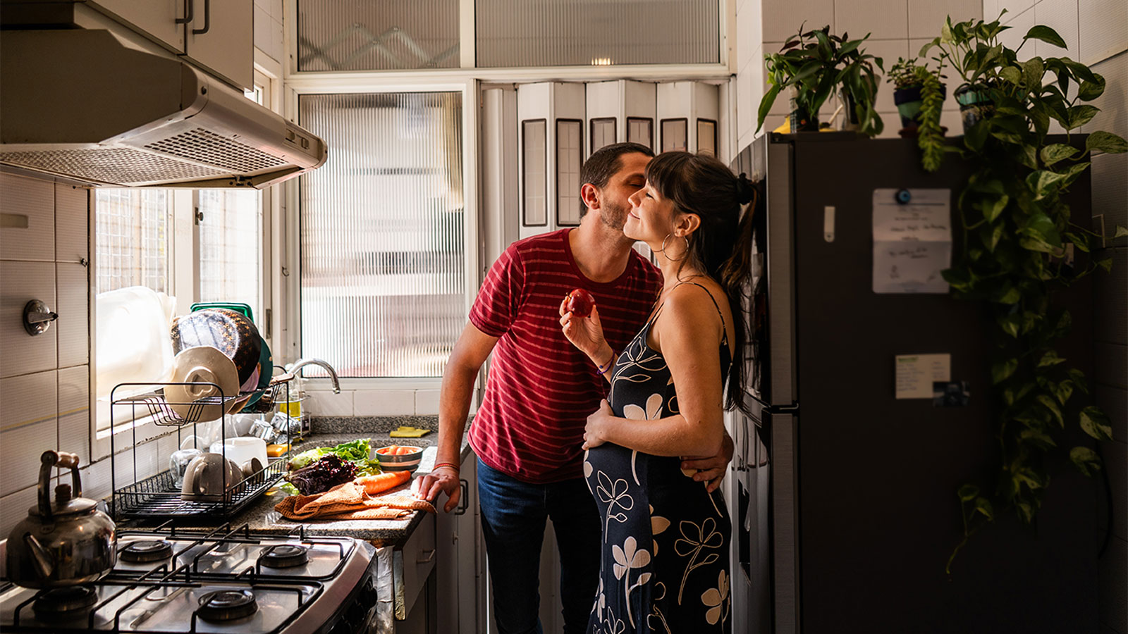 Man kisses his pregnant wife's cheek while they prepare dinner in their kitchen