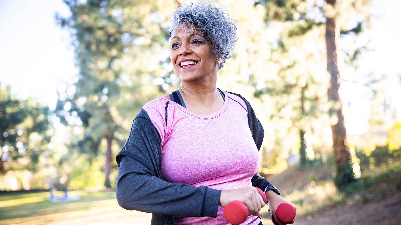 Middle aged woman holding hand weights and enjoying exercising outdoors