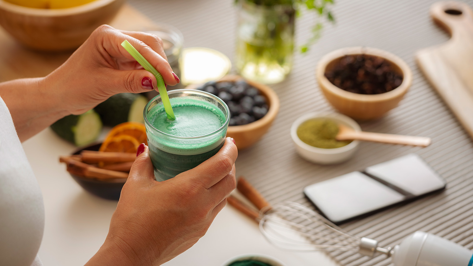 woman's hands holding a green smoothie and straw in a glass