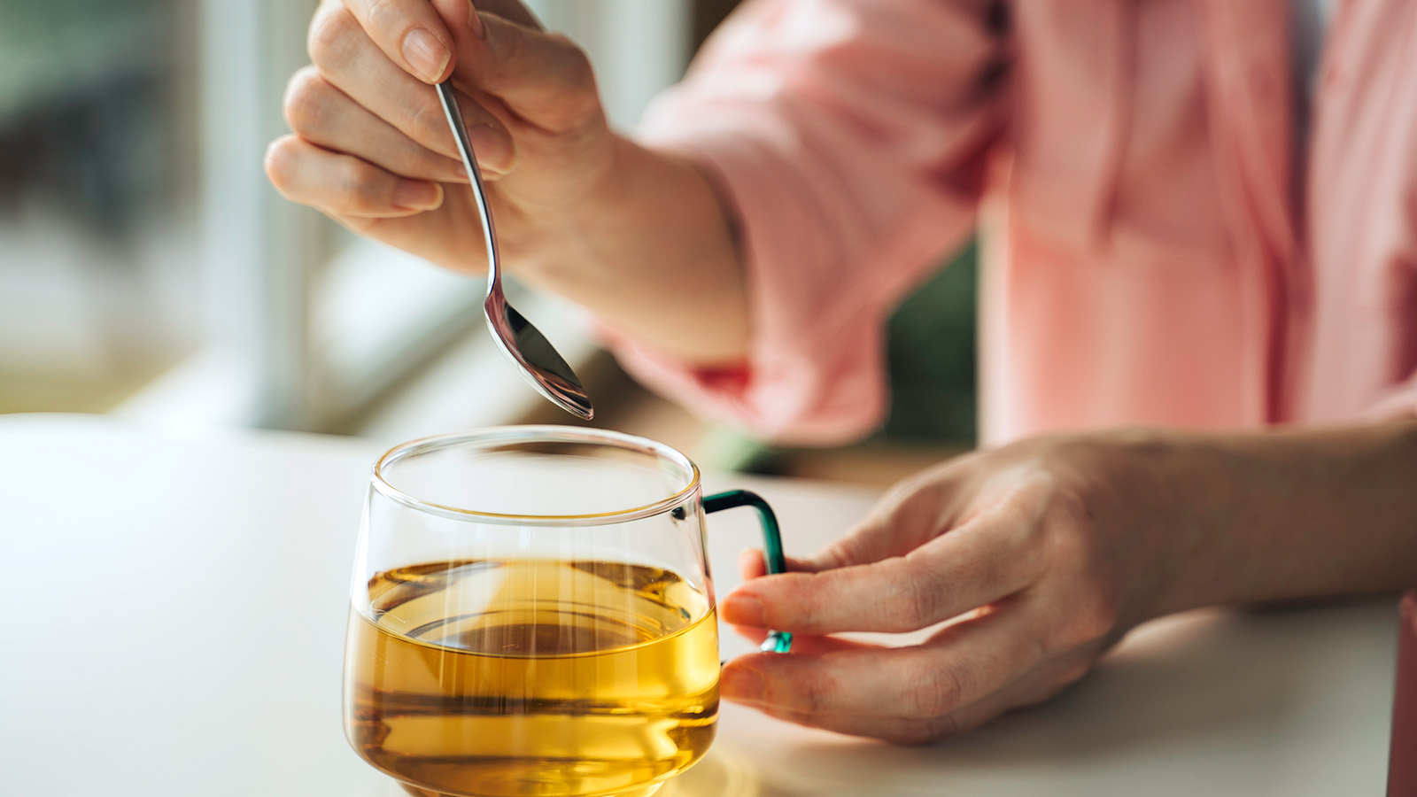 woman's hands holding a cup of herbal tea and spoon