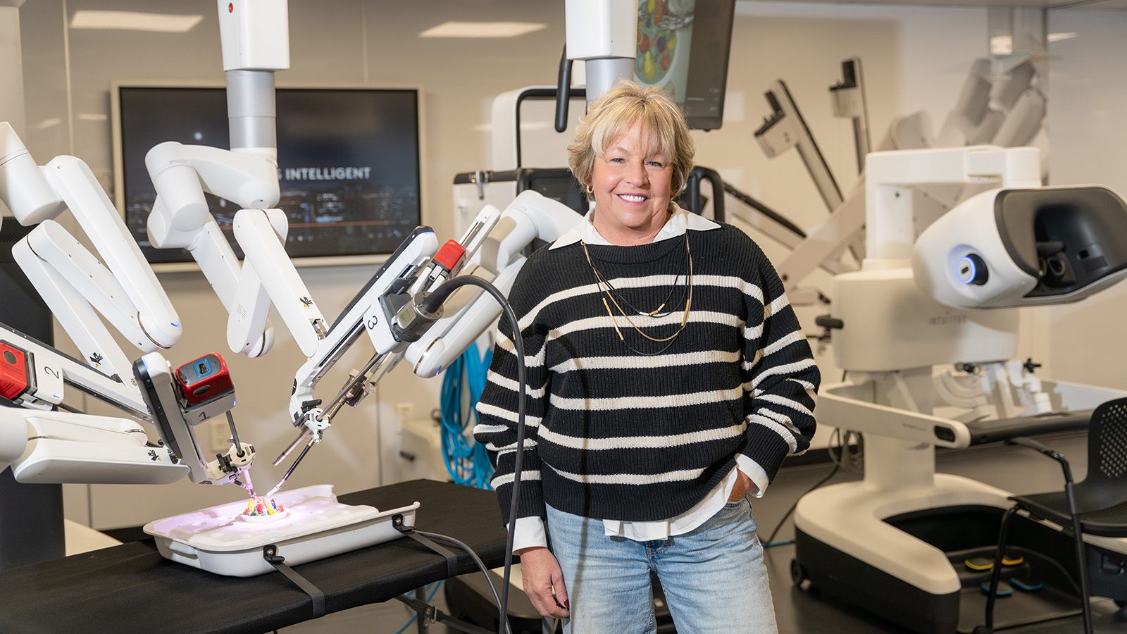 Amy, female Virtua patient who overcame lung cancer, poses with robotic surgery equipment that saved her