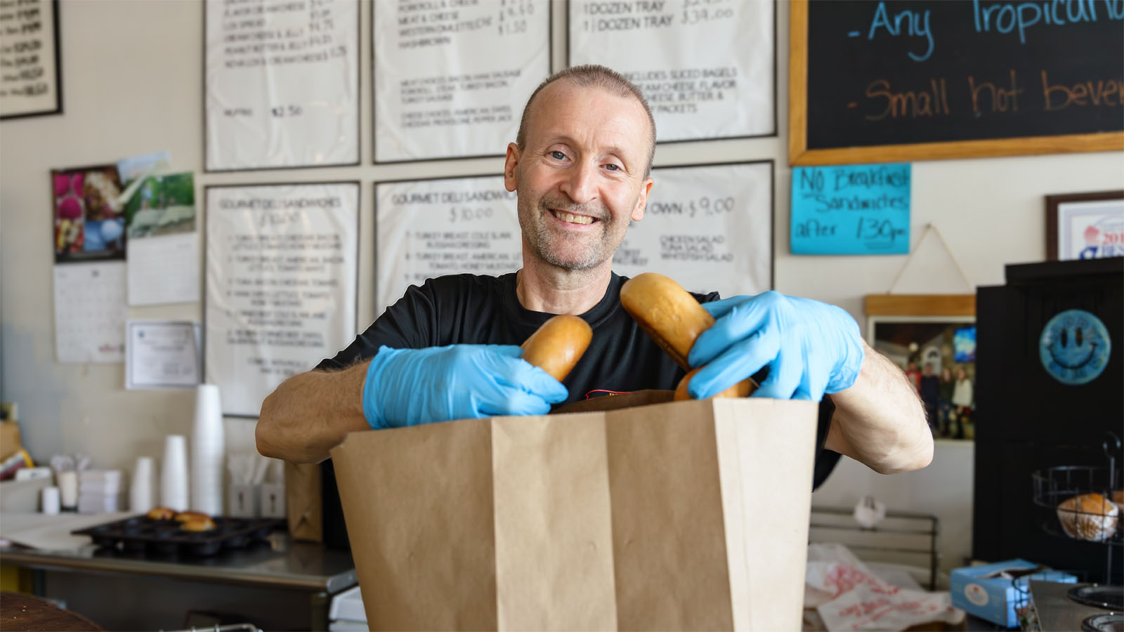 Man wearing gloves and putting bread into a paper bag at a bagel shop