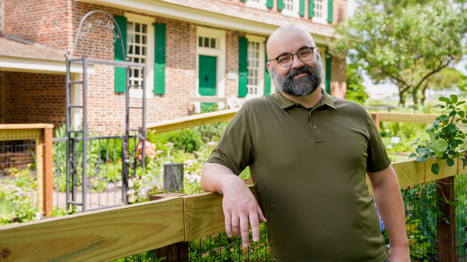 Man stands outside a home and leans against a fence