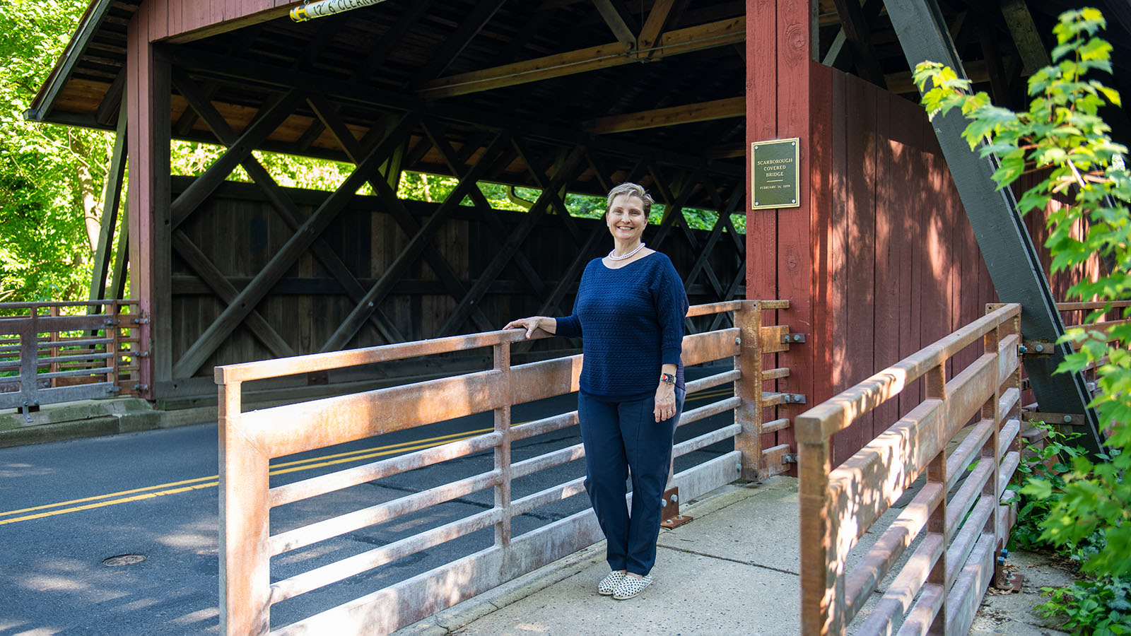 Senior woman stands on a path next to a covered bridge