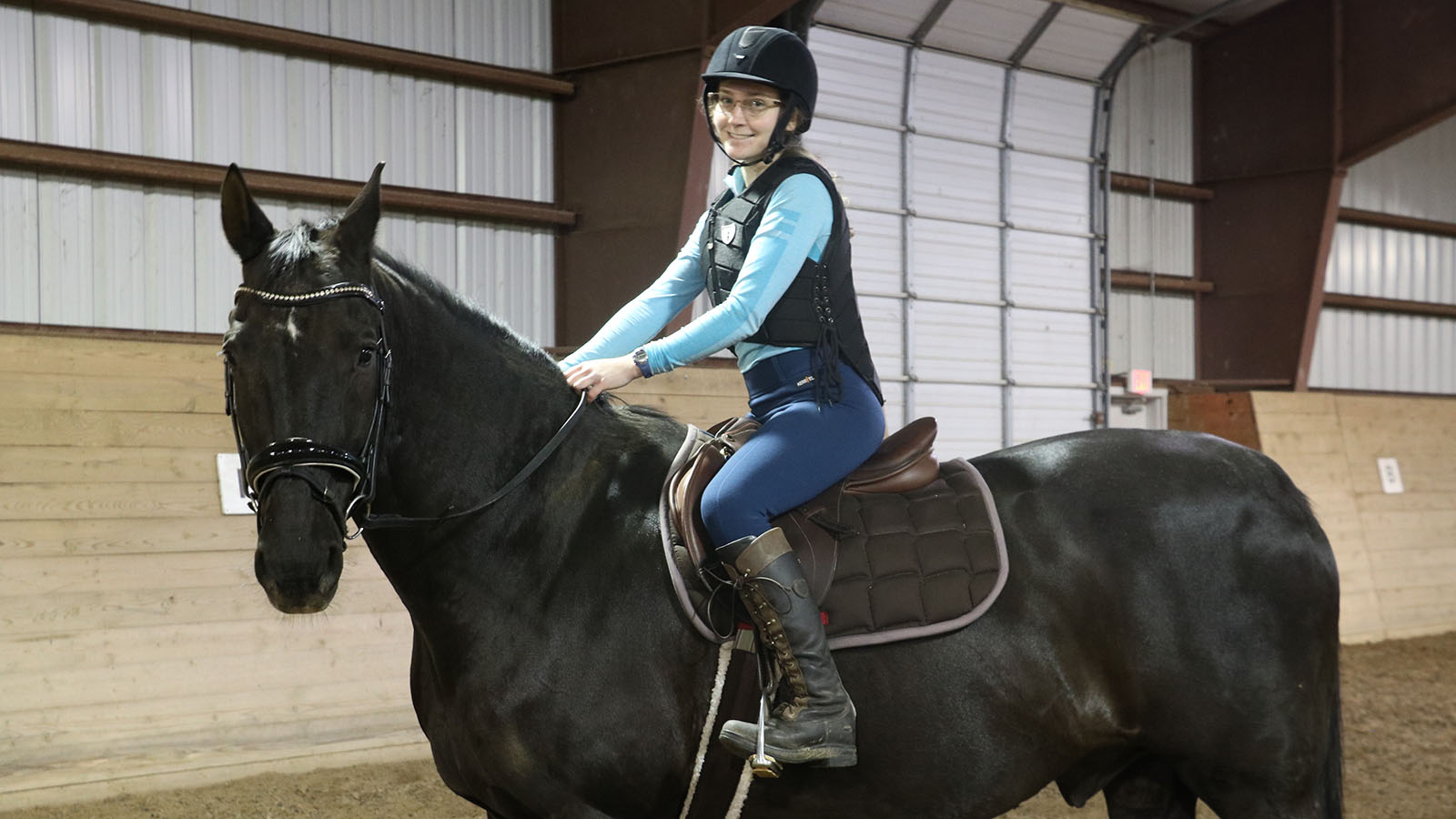 Young female equestrian posing in a barn on a black horse
