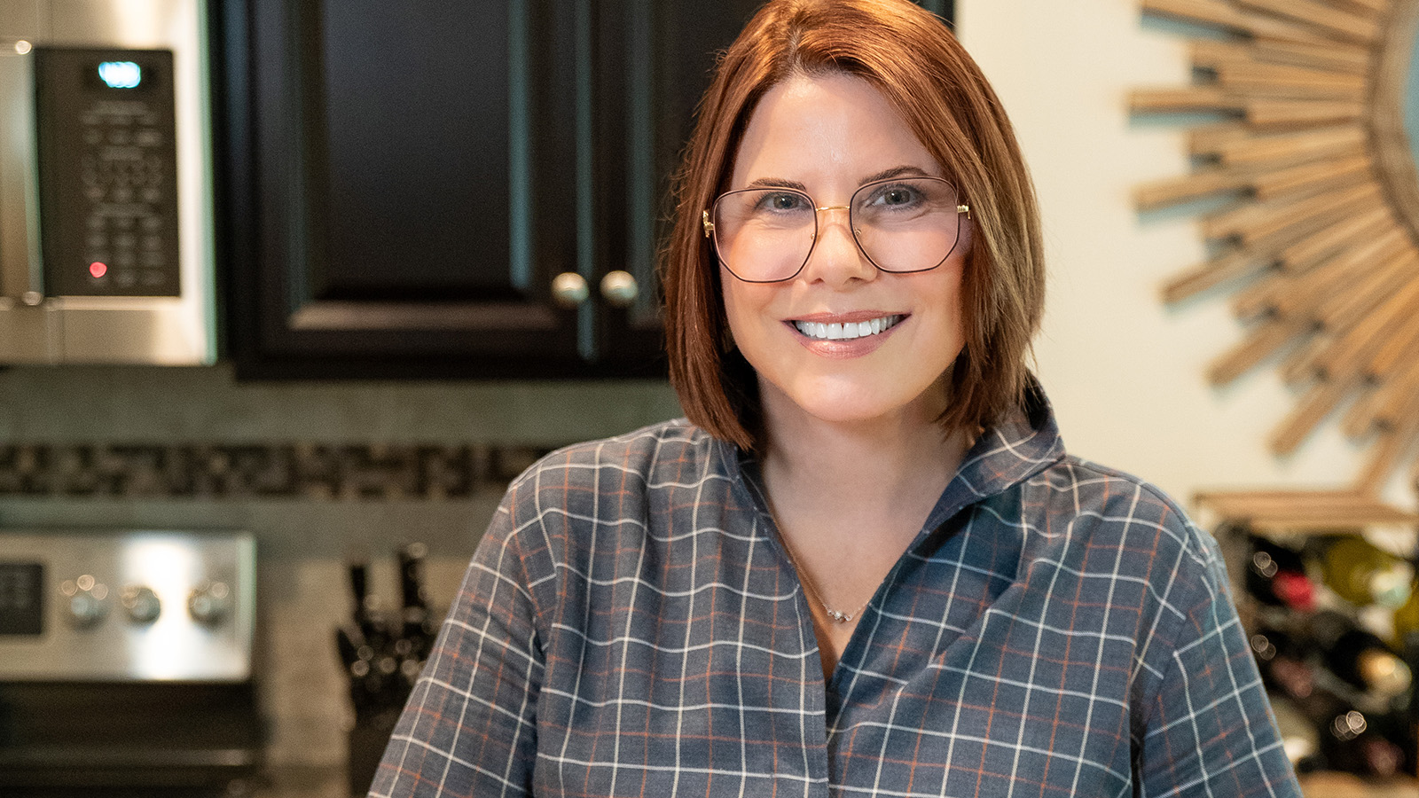 Female Virtua patient, wearing glasses, smiling, and posing in her kitchen at home.