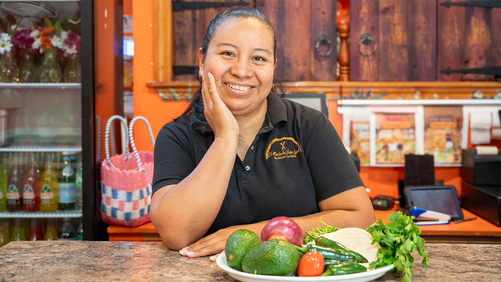 Woman smiling behind counter of Mexican restaurant with plate of fresh food