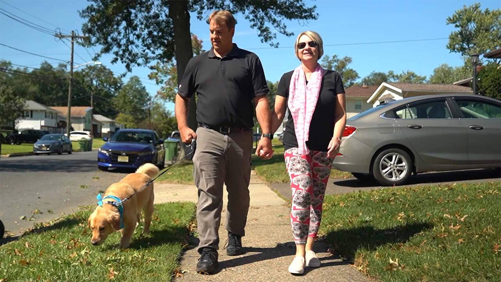 couple holding hands and walking their dog through the neighborhood