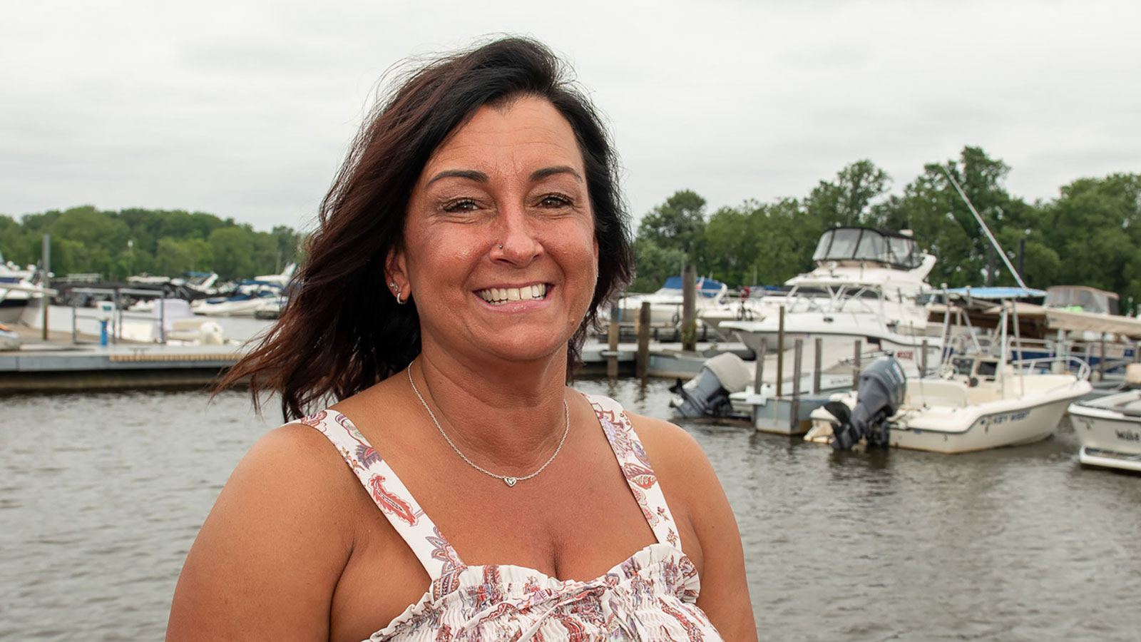 Virtua patient Tracy poses on a dock with water and boats in the background