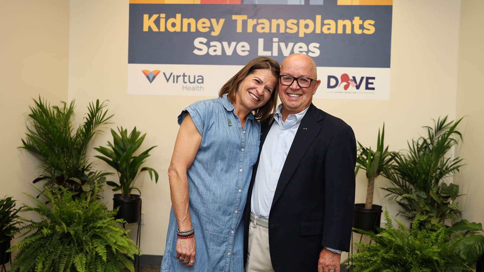 smiling woman and man standing under a Kidney Transplants Save Lives sign