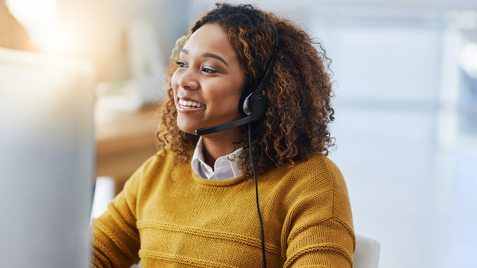 Young woman wearing headset, looking at computer and smiling