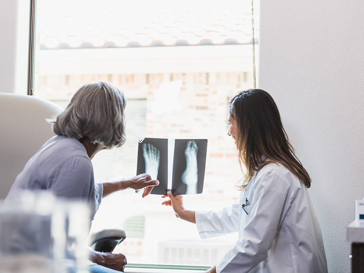 Female doctor and patient examine foot x-ray images against the window