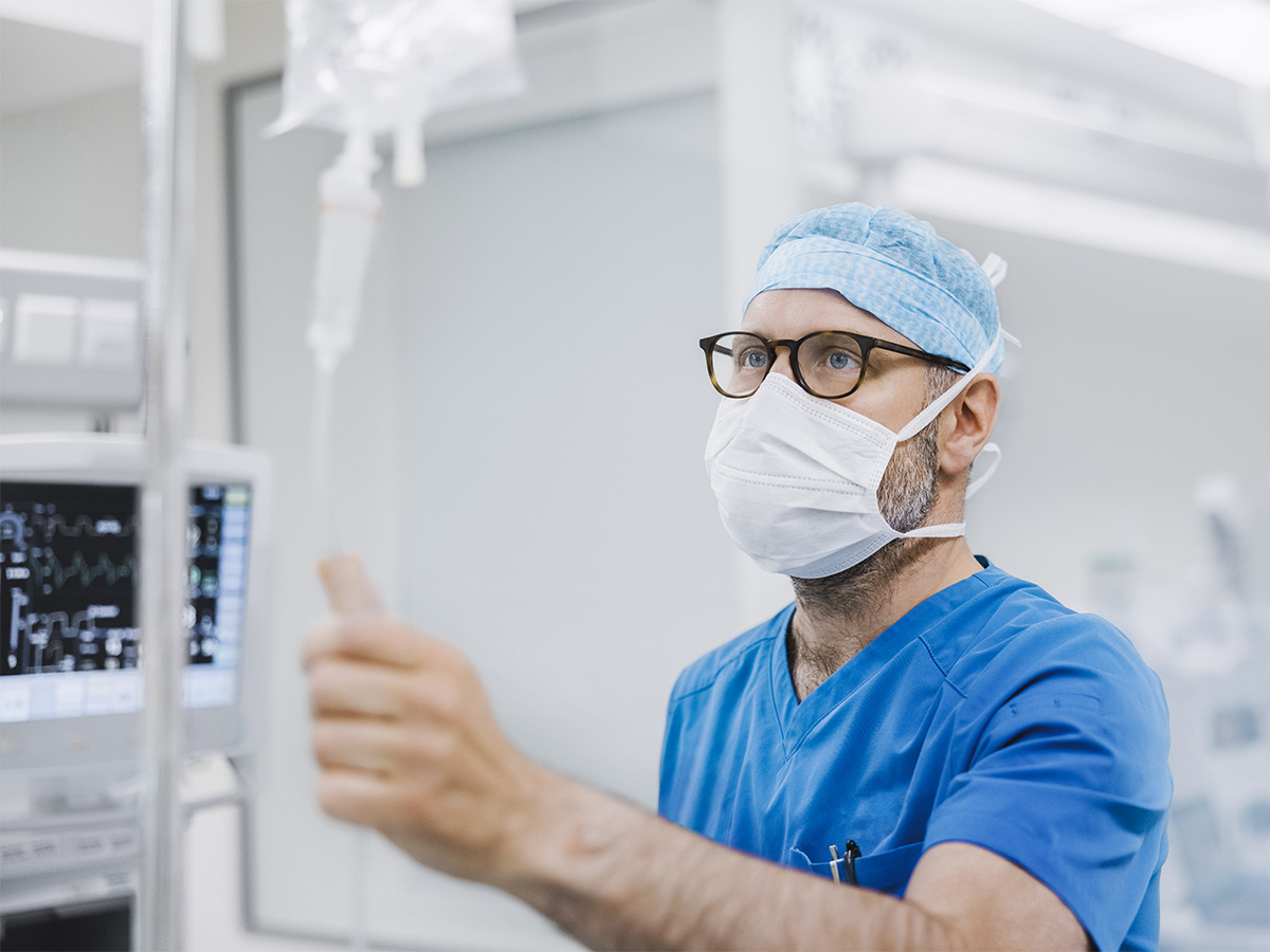 doctor wearing scrubs and mask holding the tube of an infusion bag