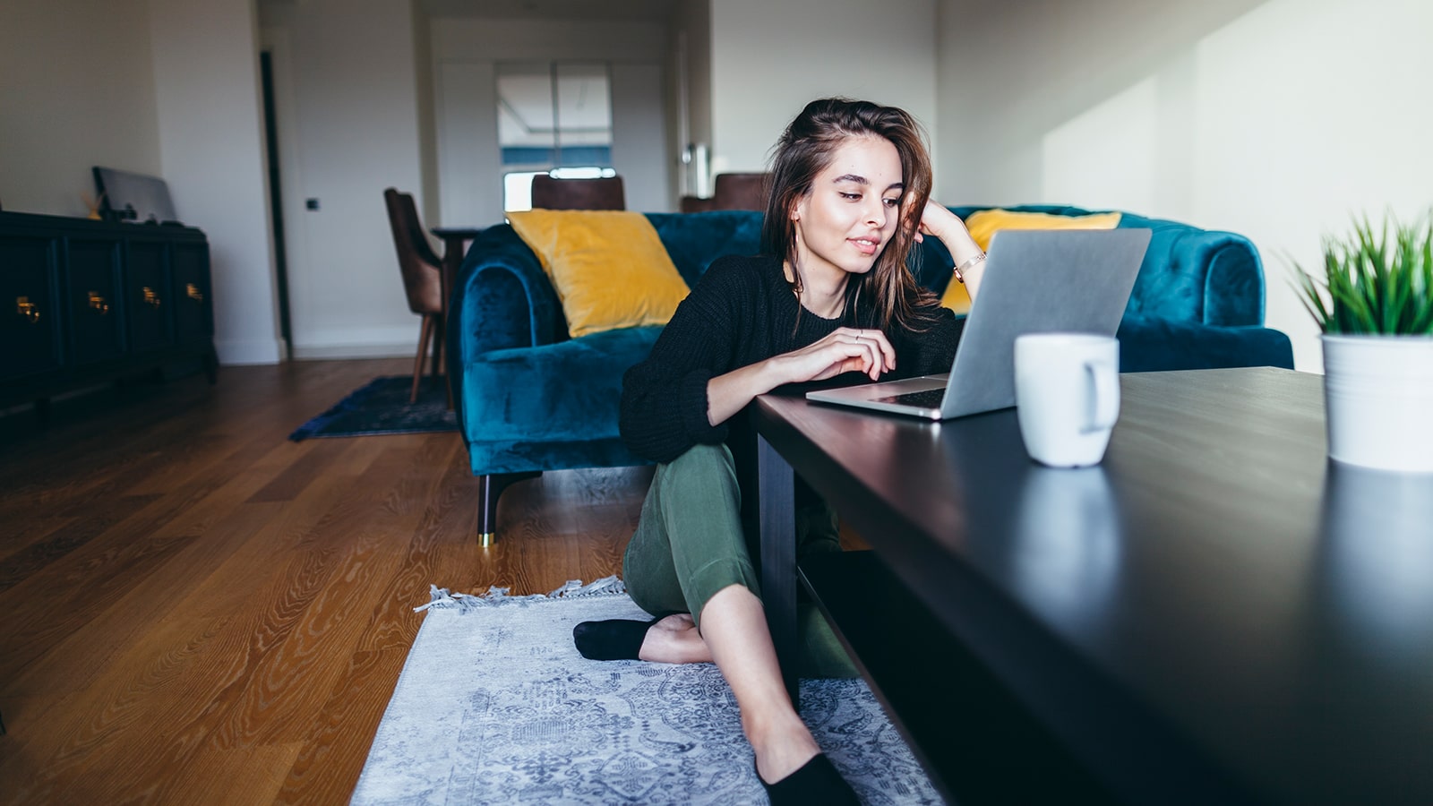 Young adult woman sits on the floor while working on her laptop