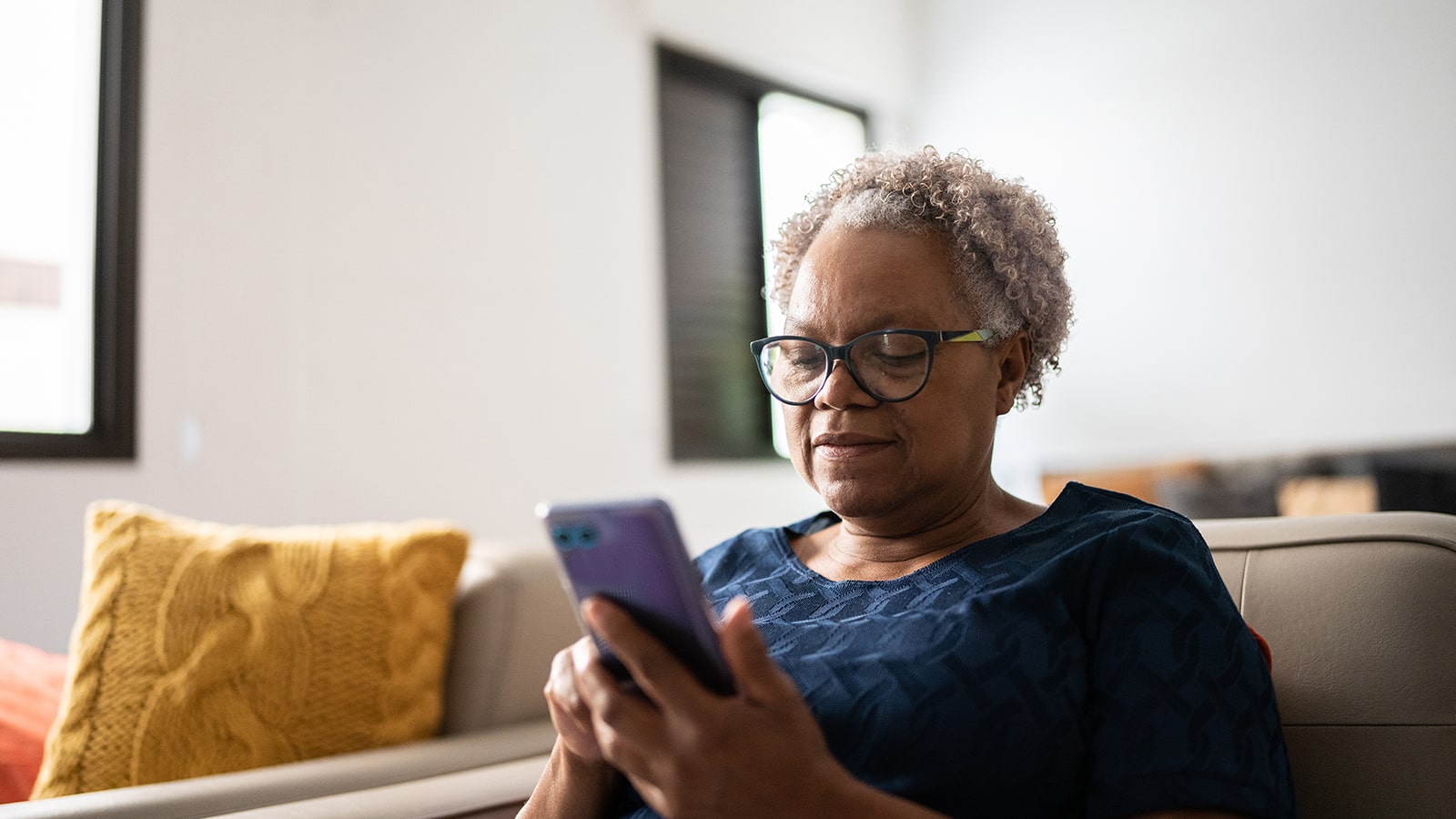 Older African American woman sits on the couch while looking at her mobile phone