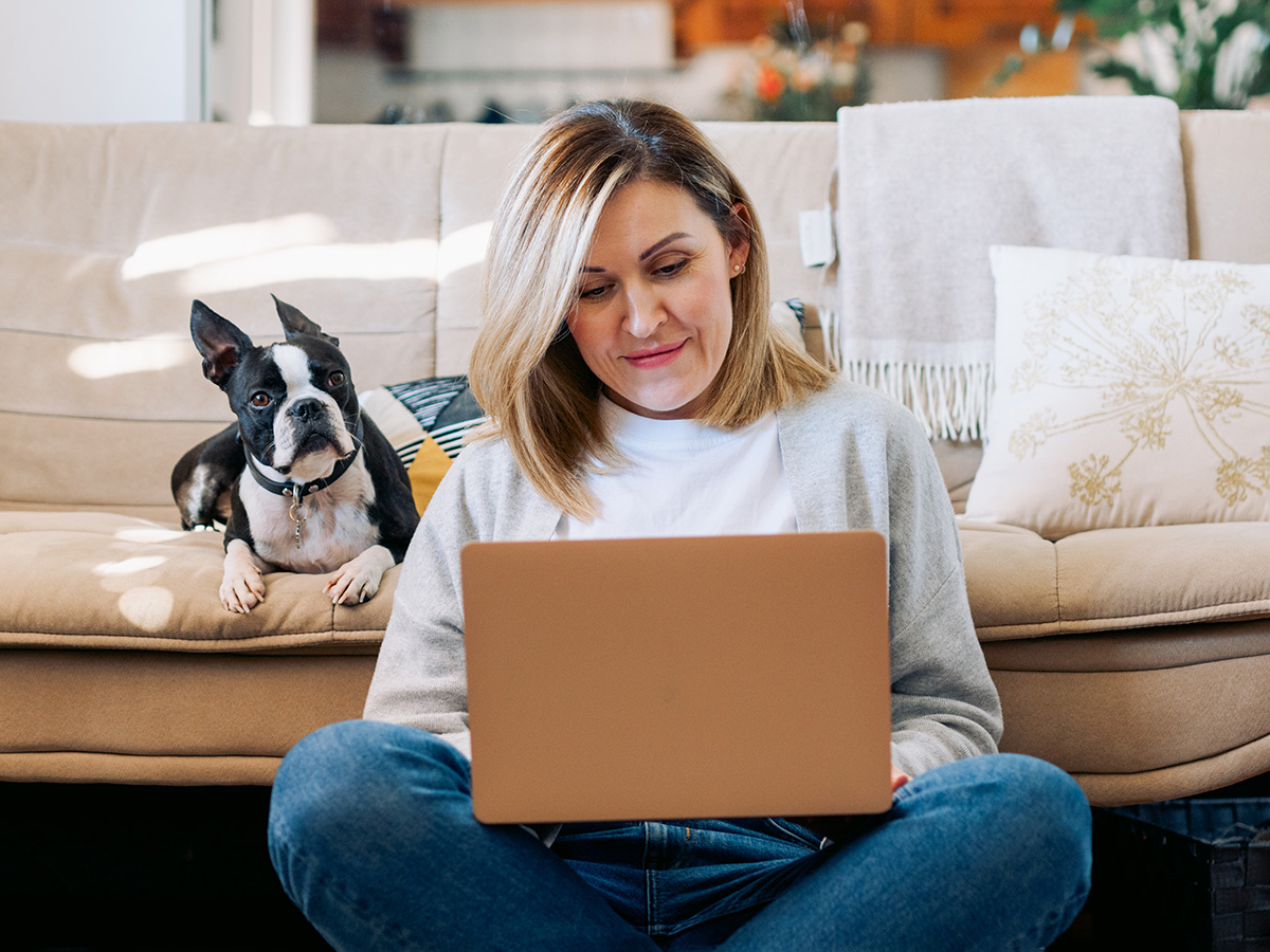 Woman sitting on the floor using the computer with her dog looking over her shoulder.