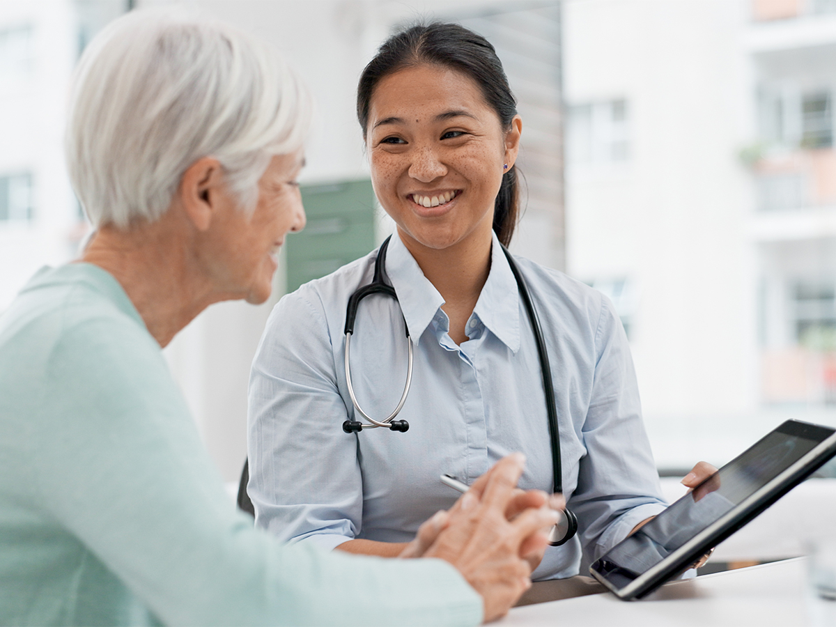 Female physician speaking with older female patient and showing her a mobile device