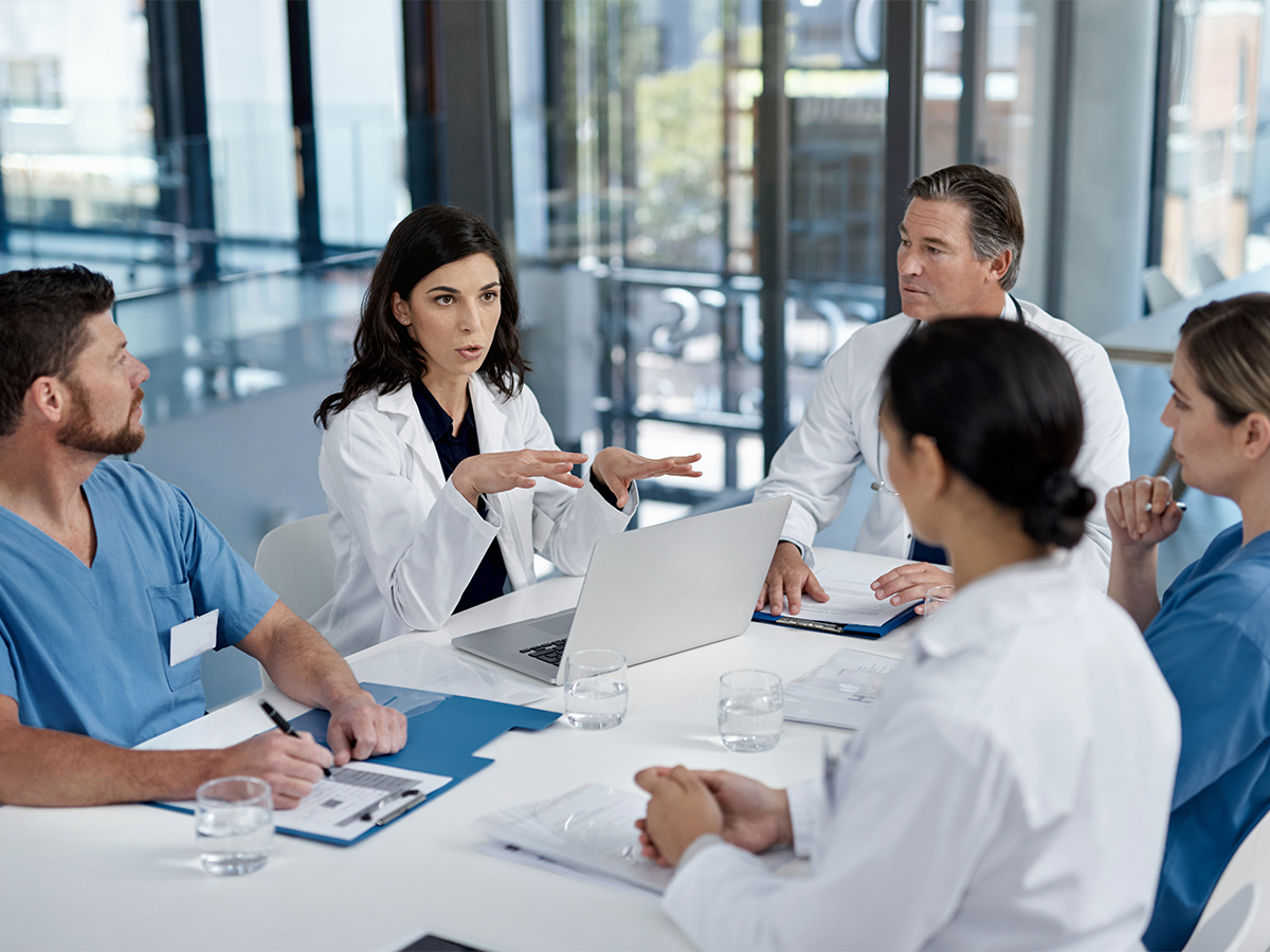 Group of male and female physicians sitting around a table with computers and patient charts