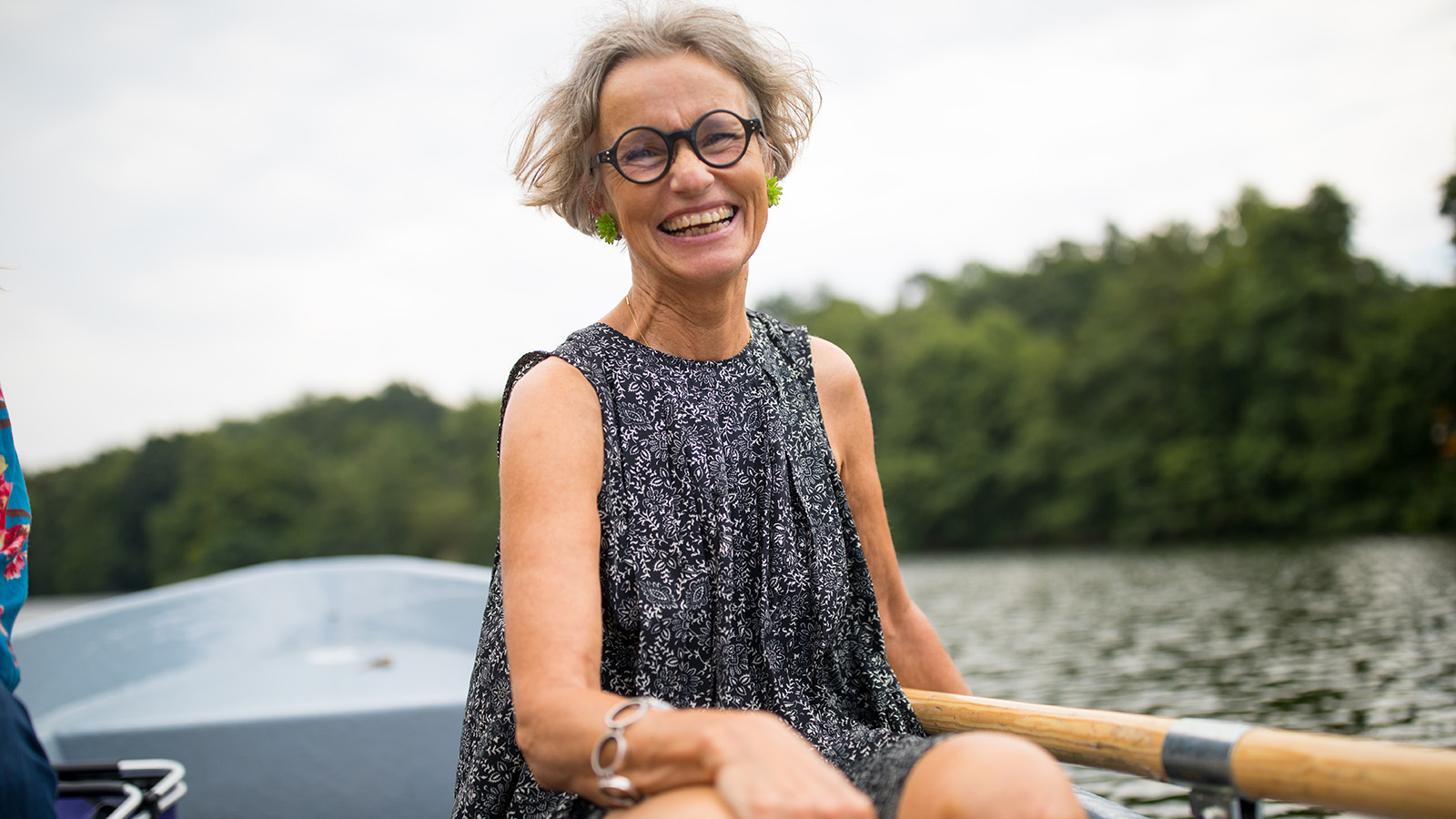 Older female adult in black shirt in a row boat on water