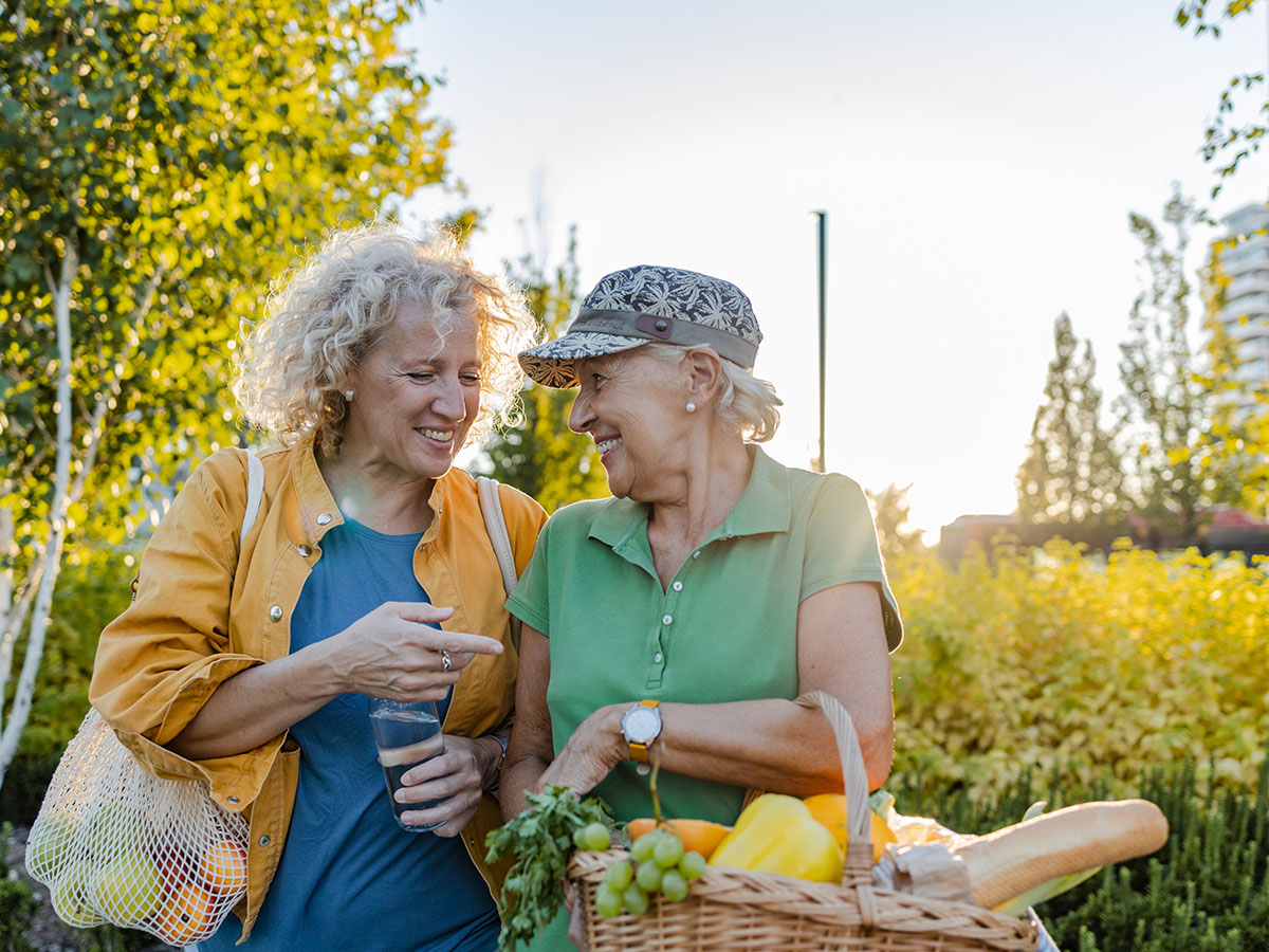 Two senior women carrying fruits and vegetables outsides.