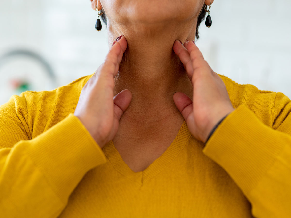 Adult woman in a yellow shirt presses her fingers against her neck