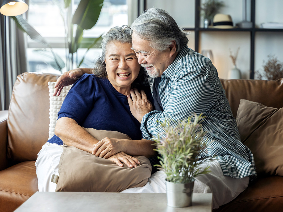Older adult couple smile and hold each other on the couch