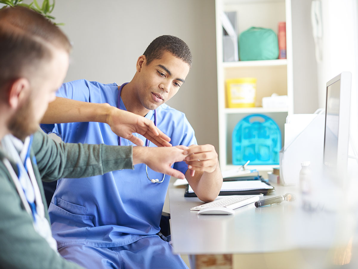 male provider in scrubs examining a male patient's hand