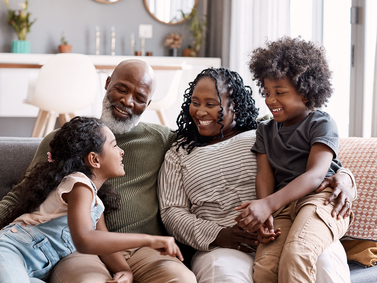 An African American family sits on the couch.