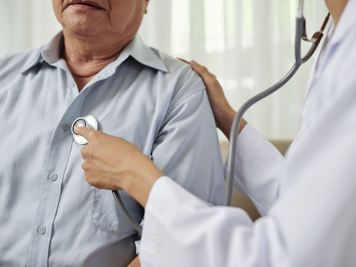 A doctor checks the heart of an older male patient.