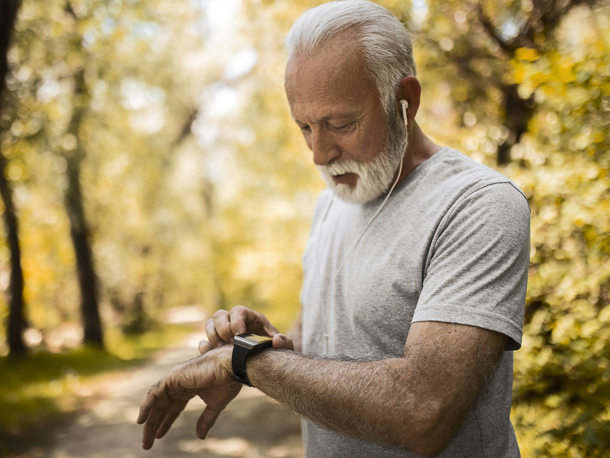 Older adult male checks his watch while exercising outdoors.
