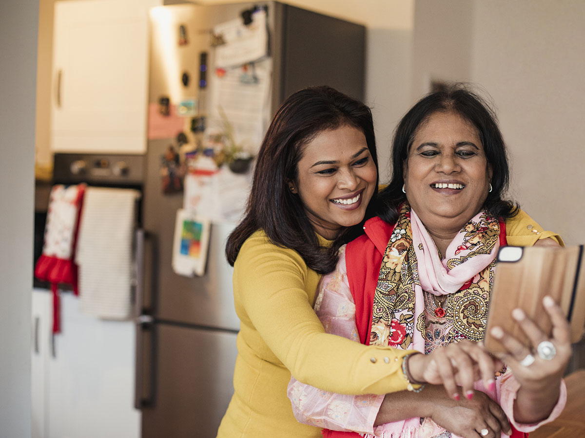 A mother and adult daughter smile while looking at a mobile phone.