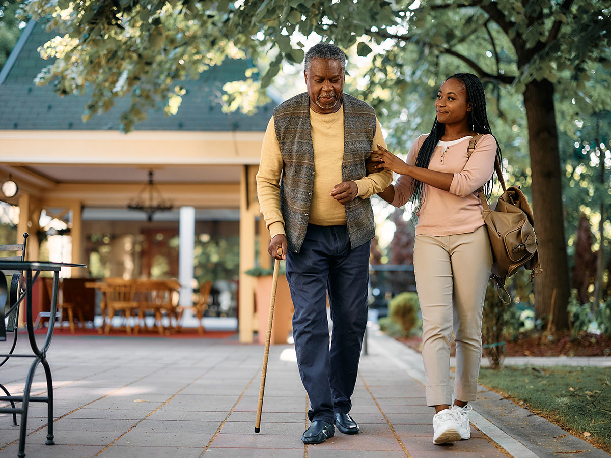 young african american woman walking with older man who uses a walking cane.