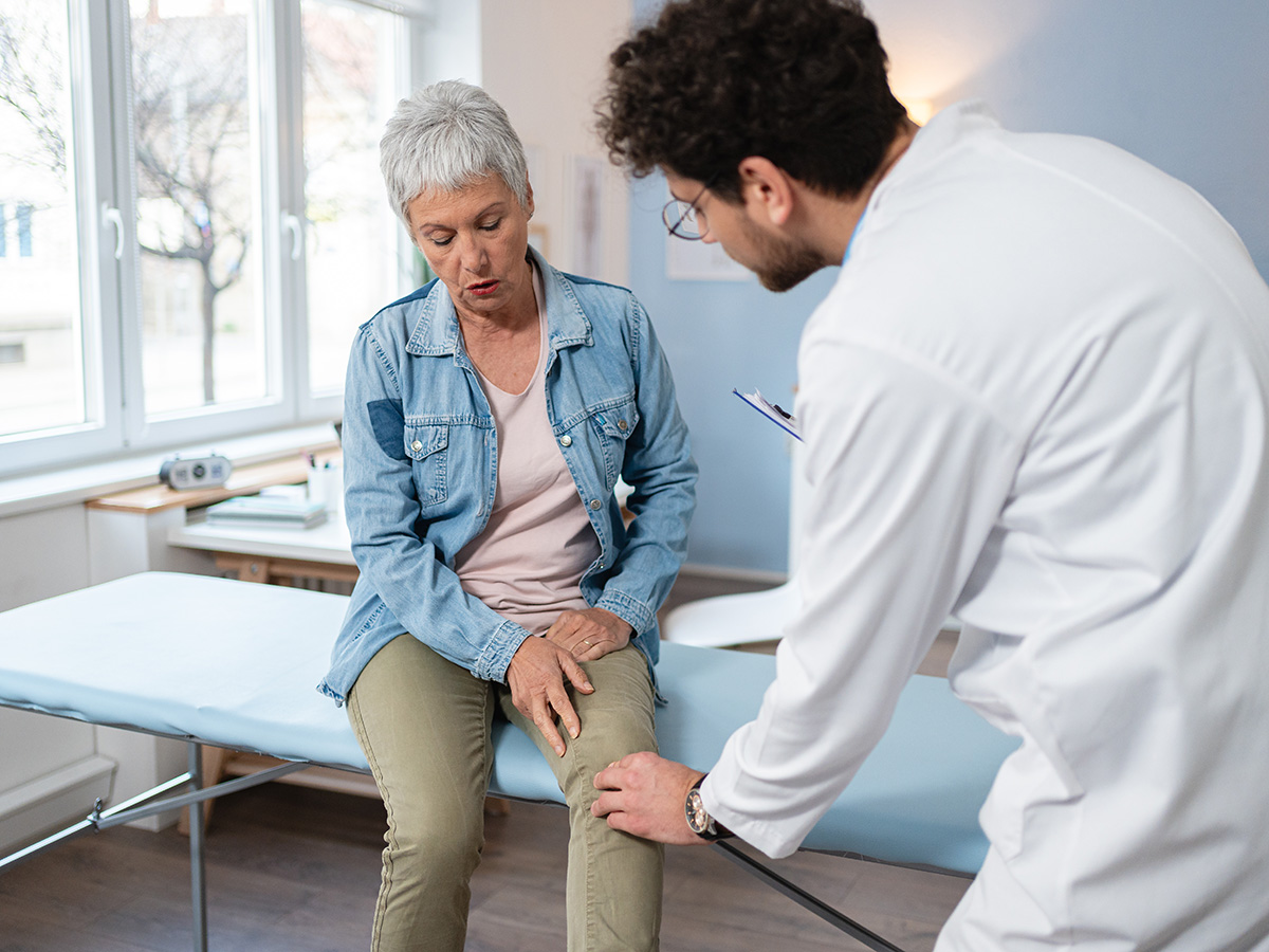 Male doctor examines the knee of a senior female patient sitting on an exam table