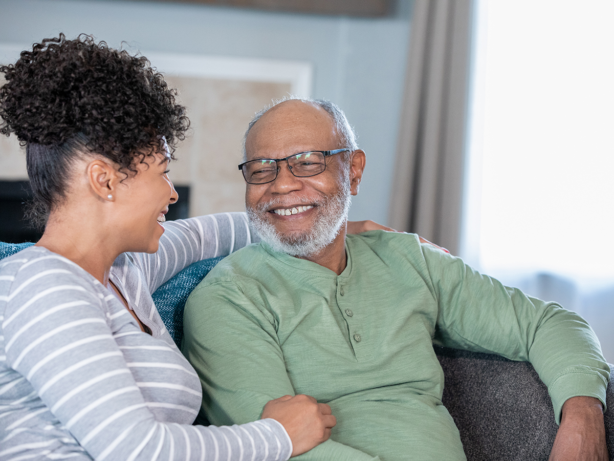 Middle aged African American Husband and Wife sitting on couch and laughing