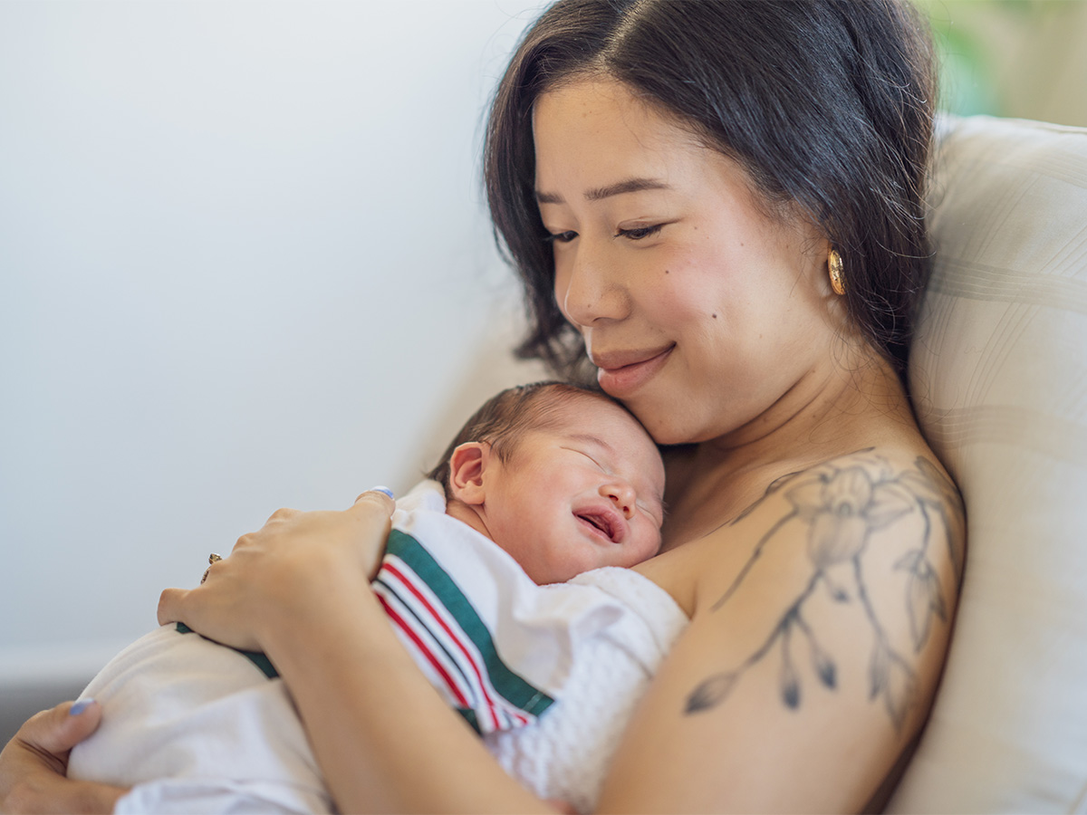 Mom with nature-inspired tattoo holding swaddled newborn