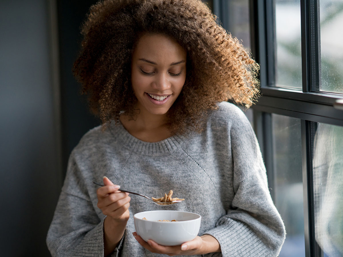 Woman eating a bowl of cereal next to a window