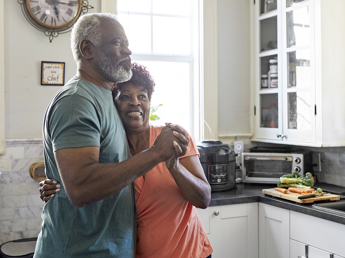 Elderly man dances with his wife in the kitchen.